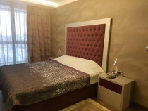 Легло и нощни шкафчета за спалня, изработени от МДФ, комбинация от естествен фурнир дъб с цвят сребърен металик и червена боя. Върху таблата на леглото има апликация от плюш.